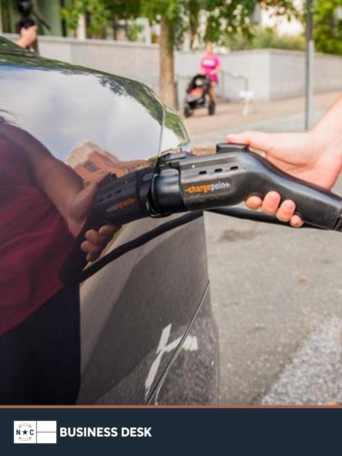 Electric vehicle charging connector at a car, with the NC Business Desk footer.