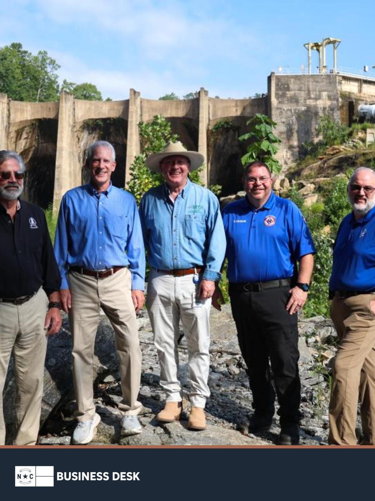 State and county officials stand in front of Turner Shoals Dam above the NC Business Desk footer.