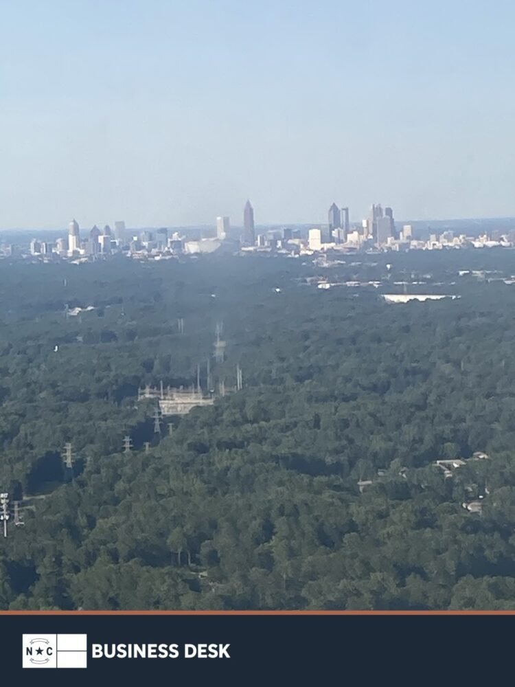 Charlotte skyline above wooded neighborhoods with the NC Business Desk footer, used for location context.