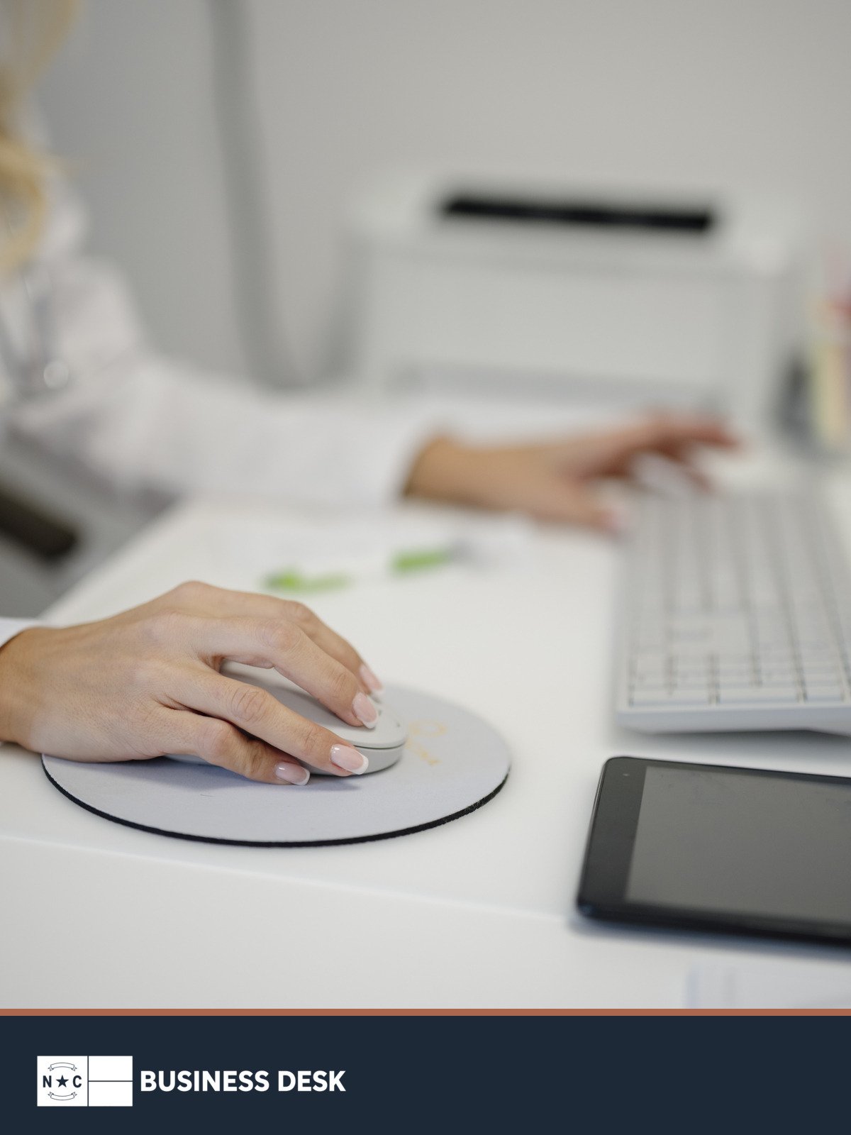 A medical professional uses a computer at a clinic desk above the NC Business Desk footer.